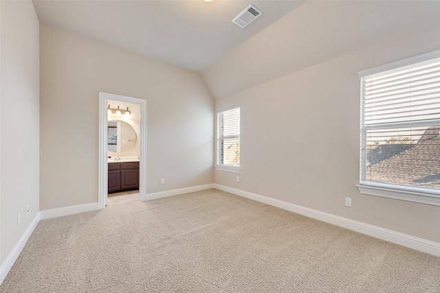 unfurnished bedroom with lofted ceiling, light carpet, visible vents, baseboards, and ensuite bath