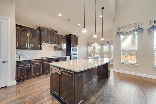 kitchen with a center island with sink, visible vents, stainless steel appliances, dark brown cabinets, and pendant lighting