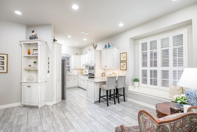 kitchen with appliances with stainless steel finishes, white cabinetry, a peninsula, and a breakfast bar area