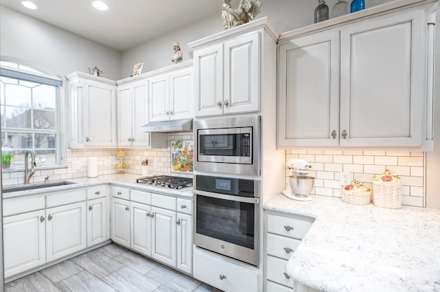 kitchen with under cabinet range hood, stainless steel appliances, a sink, white cabinetry, and tasteful backsplash