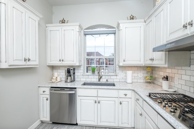 kitchen with appliances with stainless steel finishes, white cabinets, a sink, and tasteful backsplash