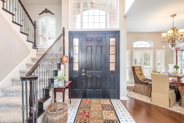 foyer entrance with baseboards, a towering ceiling, wood finished floors, stairs, and a notable chandelier