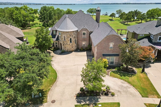 french country inspired facade with a water view, a standing seam roof, concrete driveway, and brick siding