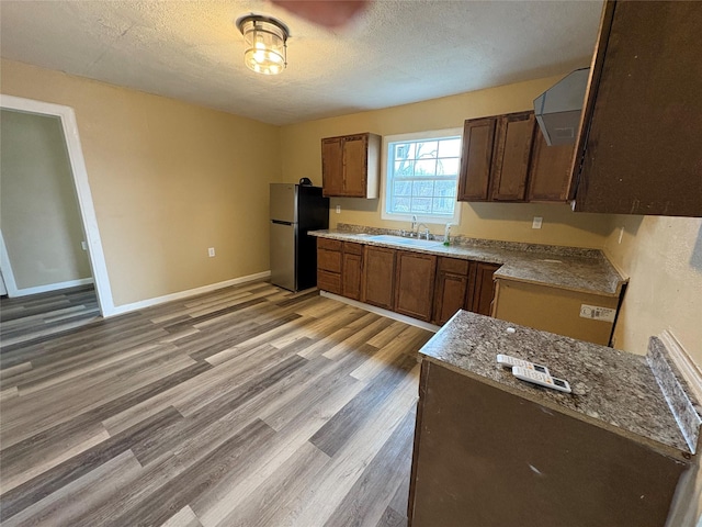 kitchen featuring a textured ceiling, a sink, light wood-style floors, freestanding refrigerator, and light stone countertops