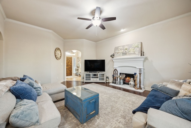 living room featuring arched walkways, dark wood-style flooring, baseboards, a lit fireplace, and crown molding