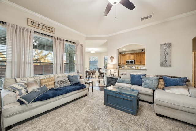 living area featuring arched walkways, ceiling fan, visible vents, light wood-style floors, and ornamental molding