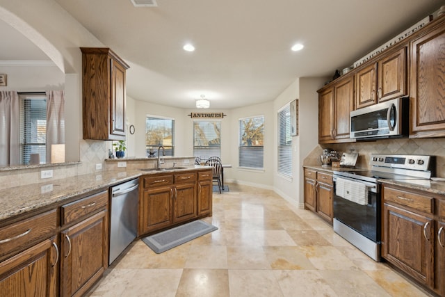 kitchen featuring appliances with stainless steel finishes, a sink, light stone countertops, and baseboards