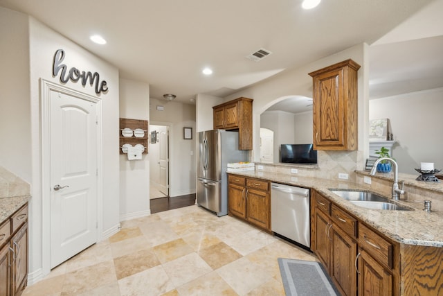 kitchen featuring brown cabinets, a sink, light stone countertops, stainless steel appliances, and backsplash