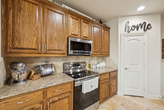 kitchen with light stone countertops, baseboards, appliances with stainless steel finishes, brown cabinets, and decorative backsplash