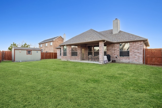 rear view of house featuring an outbuilding, a patio, a fenced backyard, a shingled roof, and brick siding