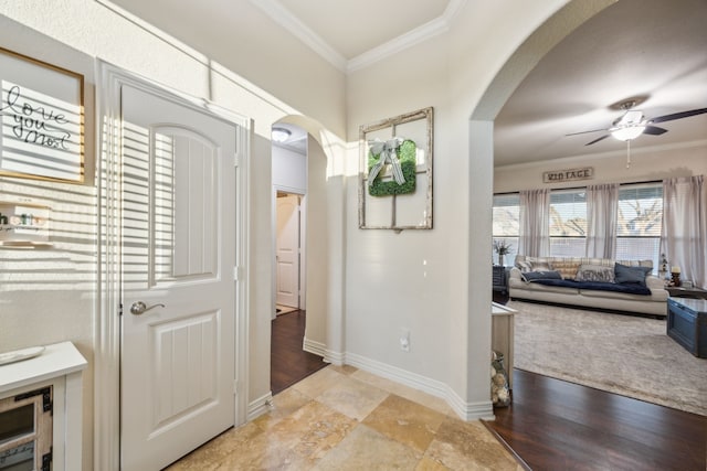 corridor featuring light wood finished floors, baseboards, arched walkways, and crown molding