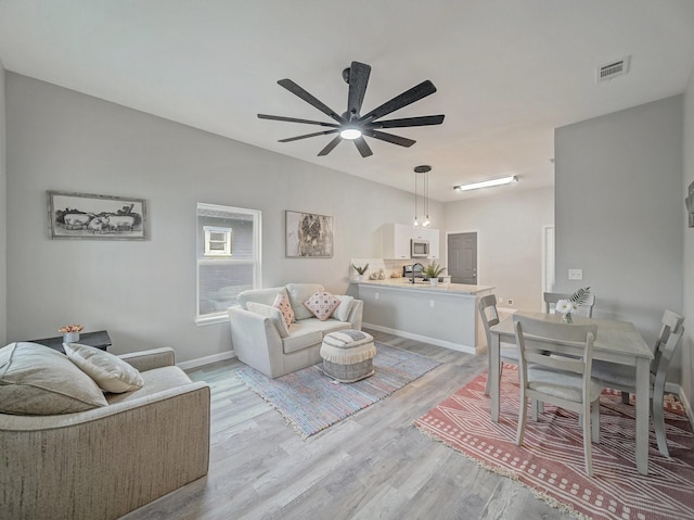 living room featuring baseboards, a ceiling fan, visible vents, and light wood-style floors