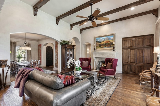 living room featuring a warm lit fireplace, visible vents, a towering ceiling, dark wood-style floors, and beamed ceiling