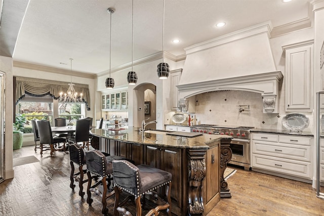 kitchen with arched walkways, custom exhaust hood, designer range, decorative backsplash, and a kitchen bar