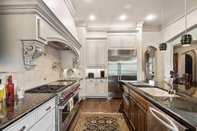 kitchen with arched walkways, tasteful backsplash, ornamental molding, a sink, and high quality appliances