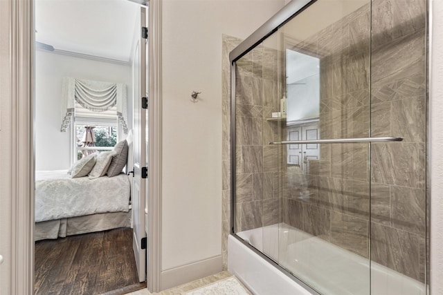 ensuite bathroom featuring baseboards, connected bathroom, wood finished floors, combined bath / shower with glass door, and crown molding