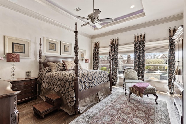 bedroom with visible vents, a ceiling fan, dark wood-style flooring, a tray ceiling, and crown molding