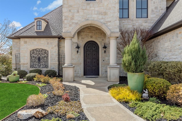 doorway to property featuring a shingled roof and stone siding