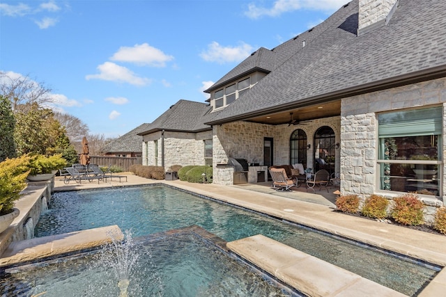 view of swimming pool with a pool with connected hot tub, a ceiling fan, a patio area, fence, and exterior kitchen