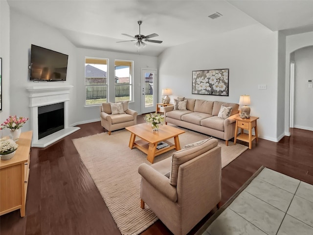 living area featuring visible vents, arched walkways, a fireplace with raised hearth, and wood finished floors