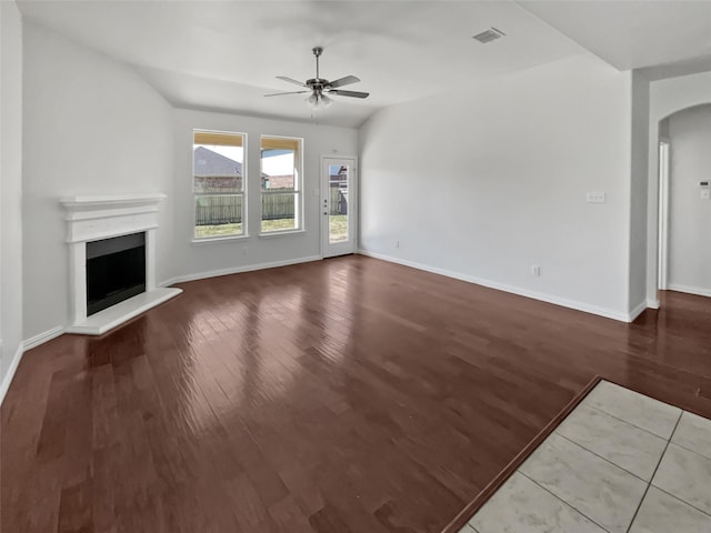 unfurnished living room with arched walkways, a fireplace with raised hearth, visible vents, and wood finished floors