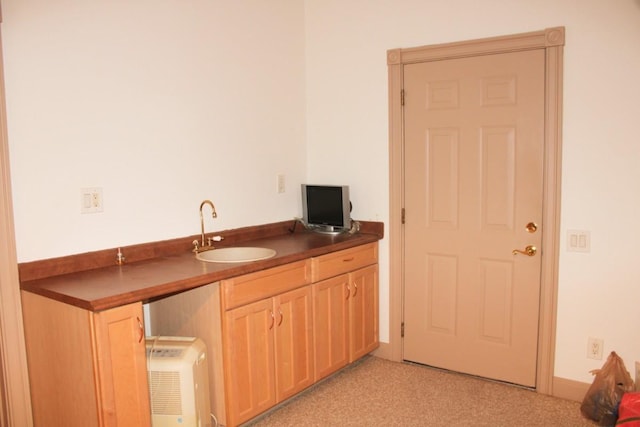 kitchen with light carpet, light brown cabinetry, dark countertops, and a sink