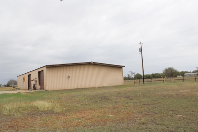 view of side of property featuring a yard, an outbuilding, a detached garage, and fence