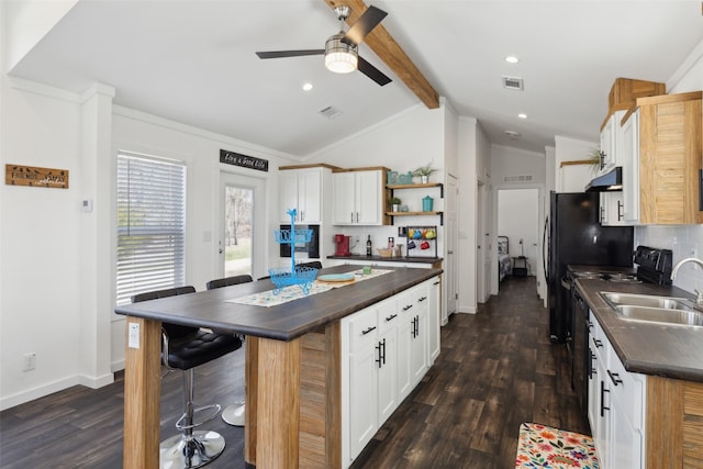 kitchen featuring dark countertops, under cabinet range hood, lofted ceiling with beams, and open shelves