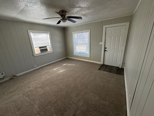 spare room with dark colored carpet, crown molding, a textured ceiling, and baseboards