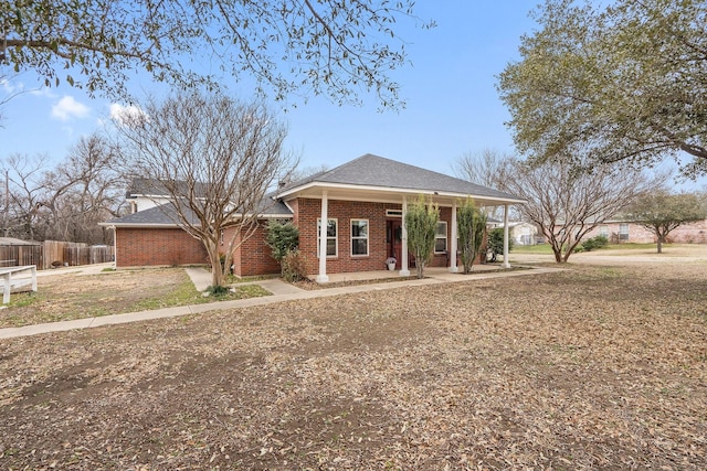 view of front of home with covered porch, brick siding, fence, and roof with shingles