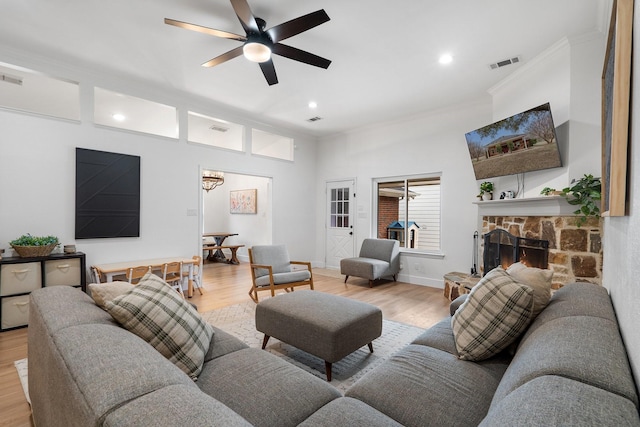 living area with visible vents, crown molding, a stone fireplace, and light wood finished floors