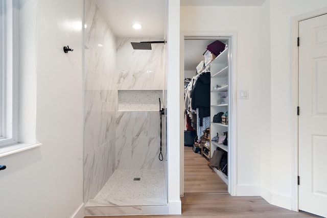 bathroom with wood finished floors, a walk in closet, a marble finish shower, and baseboards