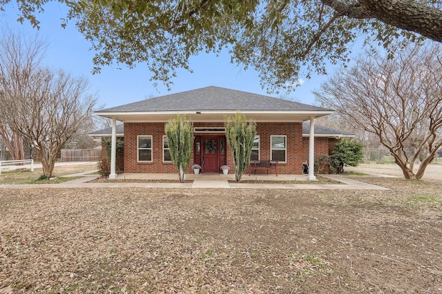 view of front of home featuring roof with shingles, fence, and brick siding