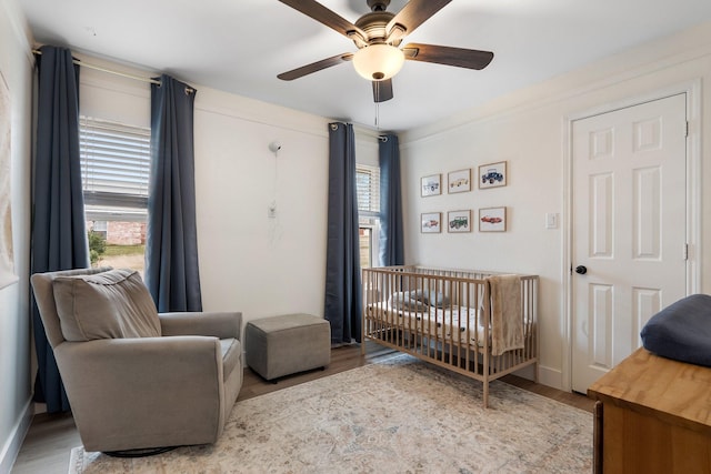 bedroom featuring a ceiling fan, a crib, and light wood finished floors