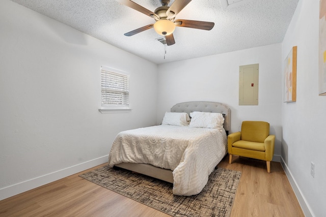 bedroom featuring light wood-type flooring, electric panel, a textured ceiling, and baseboards