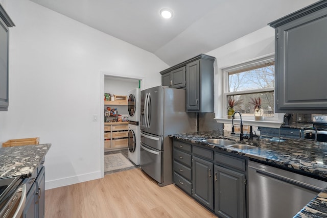 kitchen featuring stainless steel appliances, stacked washer / drying machine, gray cabinetry, vaulted ceiling, and a sink