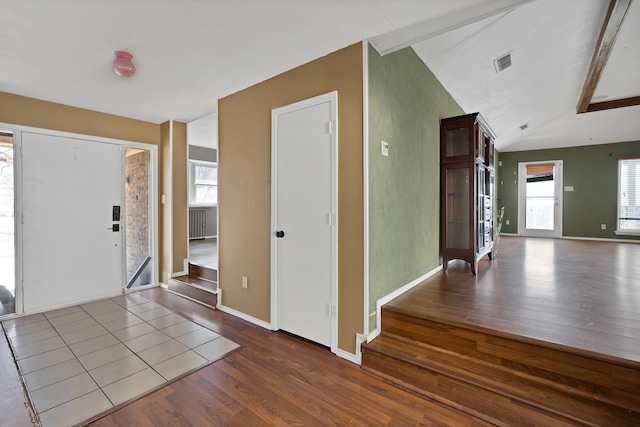 entryway featuring baseboards, visible vents, vaulted ceiling, and wood finished floors