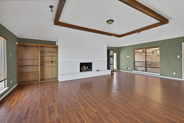 unfurnished living room featuring beamed ceiling, dark wood-style flooring, a brick fireplace, and baseboards