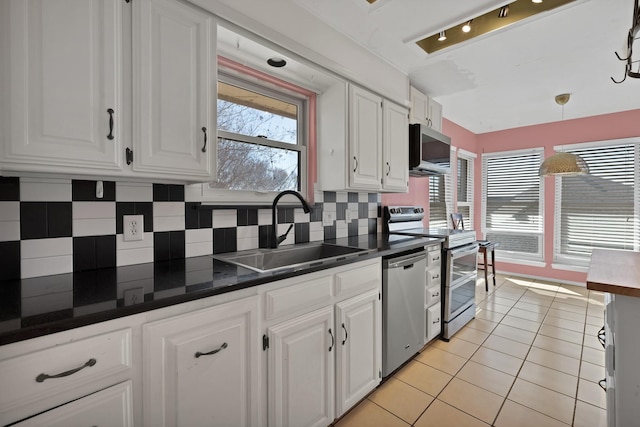 kitchen featuring light tile patterned floors, white cabinets, dark countertops, appliances with stainless steel finishes, and a sink