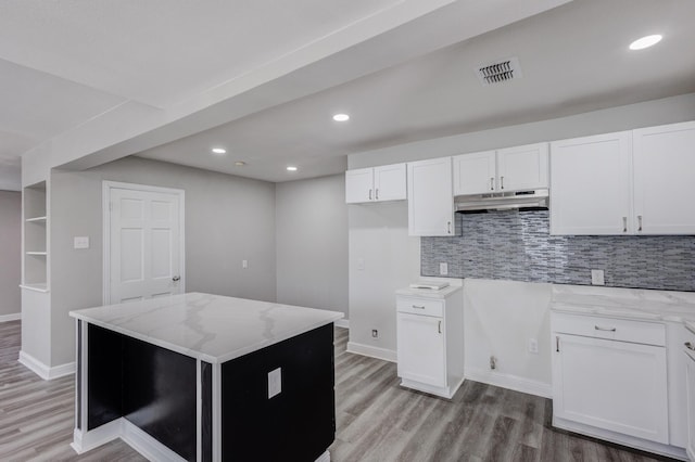 138 Whippoorwill Dr, Dallas, TX 75224 - kitchen with under cabinet range hood, light stone counters, light wood finished floors, white cabinets, and recessed lighting