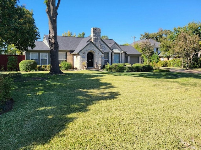 view of front of property featuring a garage, stone siding, fence, and a front lawn