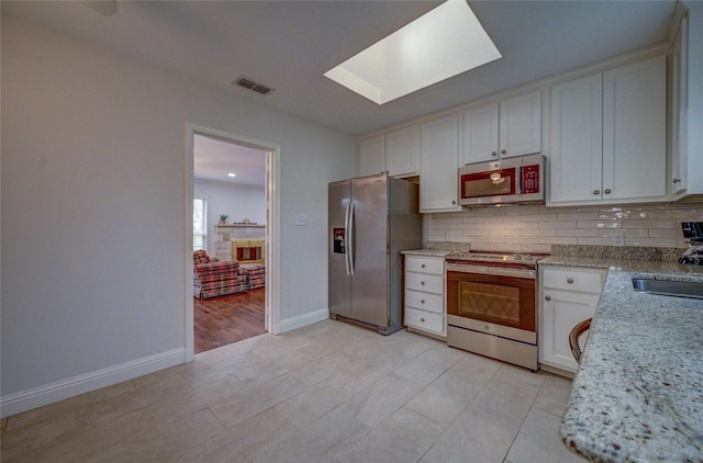 kitchen with a skylight, tasteful backsplash, white cabinets, appliances with stainless steel finishes, and light stone counters