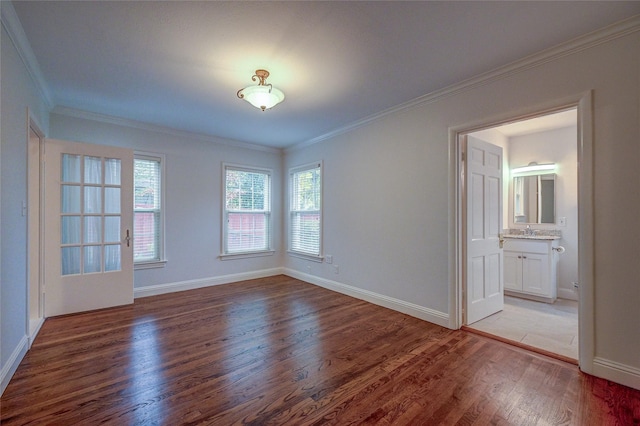 empty room featuring ornamental molding, a sink, light wood-style flooring, and baseboards