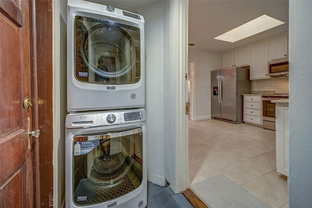 laundry room with light tile patterned floors, laundry area, stacked washer / dryer, a skylight, and baseboards