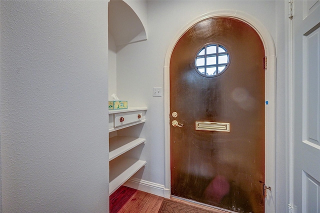 entryway featuring arched walkways, baseboards, and wood finished floors