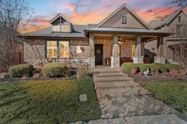 view of front of house with brick siding, a yard, covered porch, a standing seam roof, and metal roof