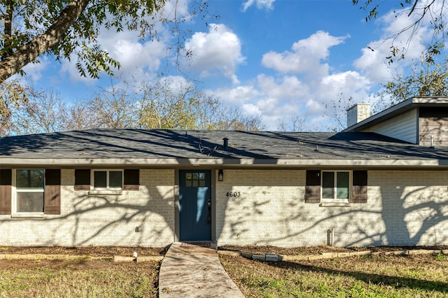 view of front of house featuring roof with shingles, a chimney, and brick siding