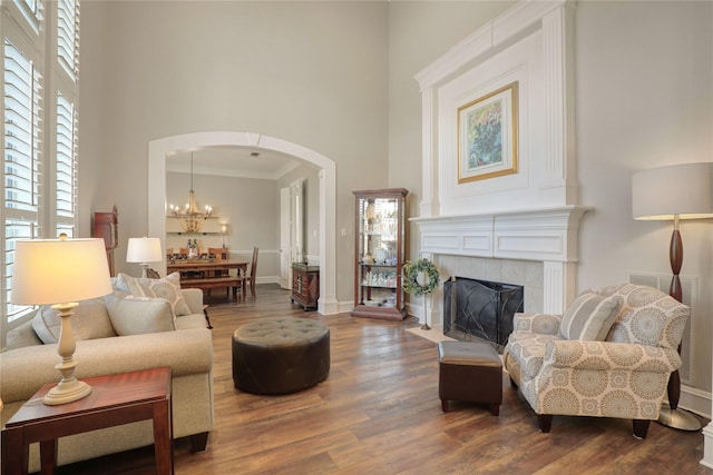 living room with baseboards, arched walkways, a tiled fireplace, a towering ceiling, and wood finished floors