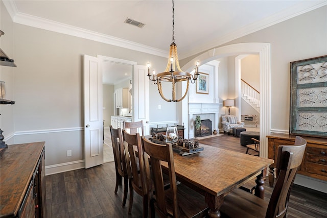 dining space featuring visible vents, arched walkways, dark wood-style floors, ornamental molding, and a lit fireplace