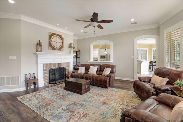 living room featuring dark wood finished floors, a fireplace, visible vents, ornamental molding, and baseboards